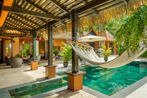 Un área de piscina con una hamaca, sillas de descanso y plantas en macetas.