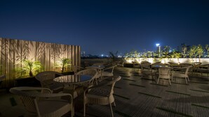 An outdoor seating area with wicker chairs and tables, surrounded by plants and a wooden partition. - Treebo Omnibliss (Dera Bassi)