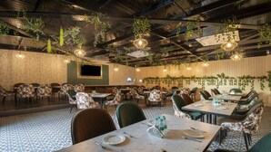 A restaurant with a high ceiling, hanging plants, and a patterned floor. Tables are set with plates and cutlery. - Treebo Omnibliss (Dera Bassi)