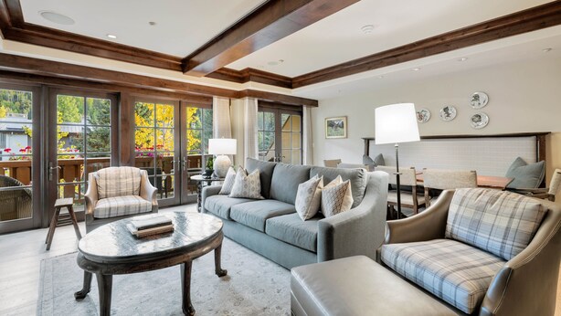 A spacious living room with a grey sofa, a coffee table, and a chair. There are large windows with curtains, a fireplace, and a lamp. - Cozy retreat at One Willow Bridge Road in Vail Village (Vail)