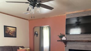 A living room with a ceiling fan, a fireplace, a sofa, and a coffee table. - Cozy up at Foxtrot Inn! 
Immaculate! Outdoor Grain Bin BBQ area! Dog friendly!  (Cunningham)