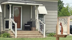 A building with a porch, a sign for Foxtro Inn, and a number 214 on the door. - Cozy up at Foxtrot Inn! 
Immaculate! Outdoor Grain Bin BBQ area! Dog friendly!  (Cunningham)