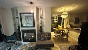 A modern living room with a fireplace, a dining area with a chandelier, and a kitchen visible through an open door. - Penthouse with Large Deck on Seawall / Beach w/ Views (Vancouver)