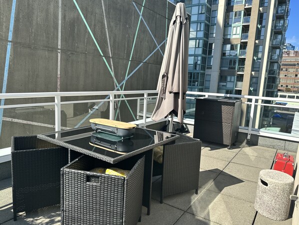Terraza en la azotea con una mesa, sillas y un cubo de basura.