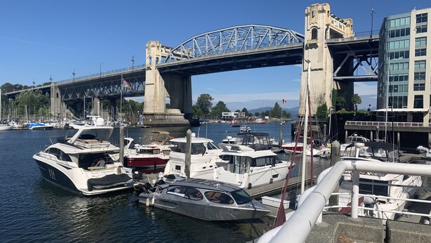A marina with boats docked under a bridge, a waterfront building, and a clear sky. - Penthouse with Large Deck on Seawall / Beach w/ Views (Vancouver)