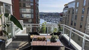 A balcony with a table and chairs, a potted plant, and a view of a marina and cityscape. - Penthouse with Large Deck on Seawall / Beach w/ Views (Vancouver)