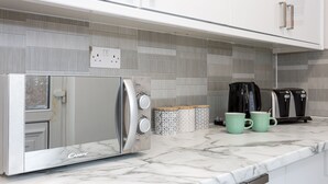 Una cocina con microondas integrado, cafetera y dos tazas sobre la encimera.