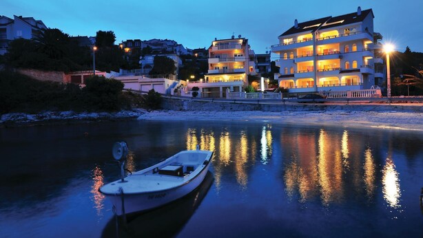 Ein Anwesen am Wasser mit einem vor Anker liegenden Boot, das die beleuchteten Gebäude im Hintergrund reflektiert.