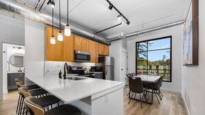 Una cocina moderna con una isla central, taburetes de bar y un comedor con un amplio ventanal.