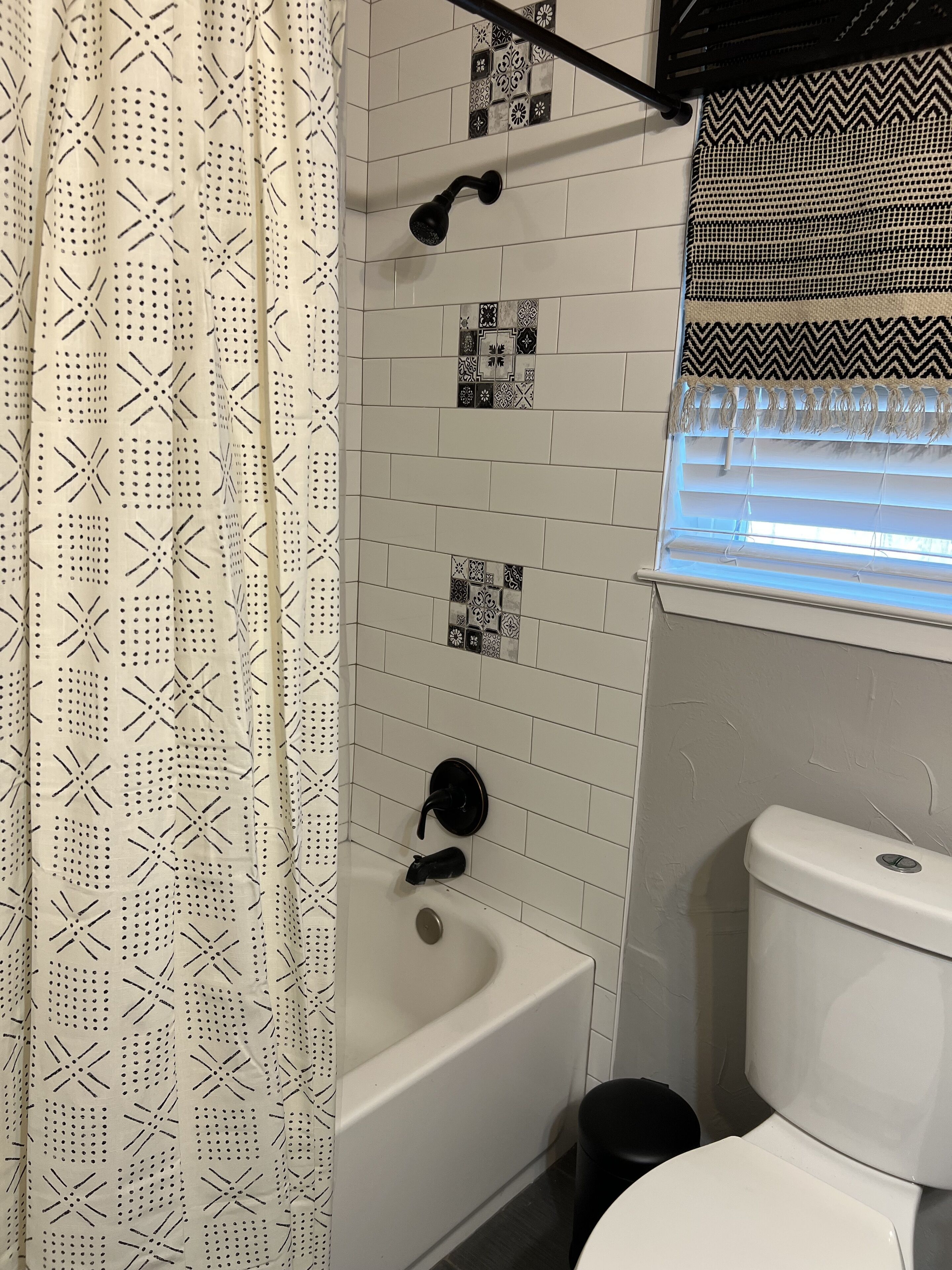 A bathroom with a white bathtub, a toilet, and a shower curtain with a geometric pattern.