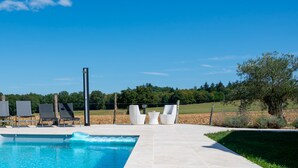 Una piscina con sillones de descanso y fuente, rodeada de césped y árboles.