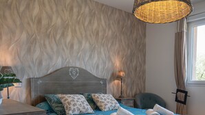 Un dormitorio con cama, mesita de noche, lámpara, silla y ventana con cortinas.