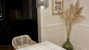 Comedor con una mesa de mármol, sillas de mimbre, un jarrón con plumas de plumas y luces colgantes.