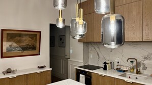 Una cocina moderna con armarios de madera, encimera de mármol y lámparas colgantes con bombillas a la vista.