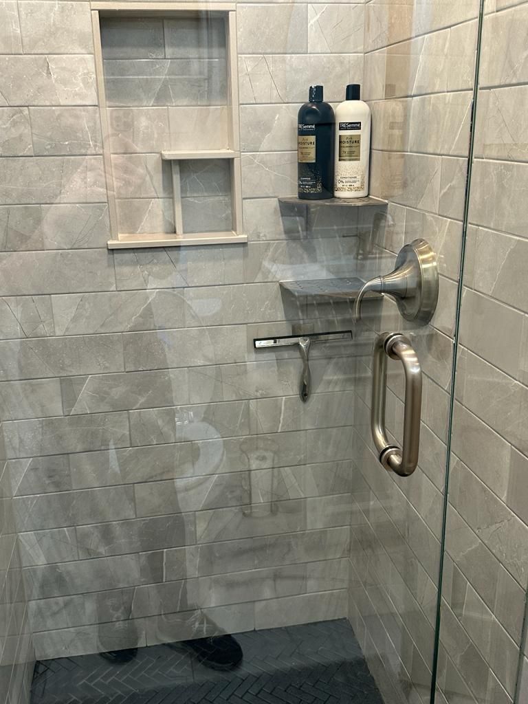 A shower area with a glass door, a handrail, and two bottles of shampoo on a shelf.