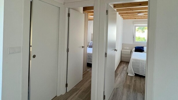 A hallway with wooden beams, white doors, and a bed with a blue pillow in the adjacent room.