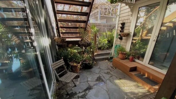 Un patio con suelo de piedra, un banco de madera y plantas en macetas.