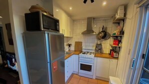 Cocina compacta con refrigerador, estufa, microondas y salpicadero de azulejos blancos.