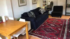 Una sala de estar con un sofá azul oscuro, una mesa de madera, un tapete rojo estampado y una estantería.