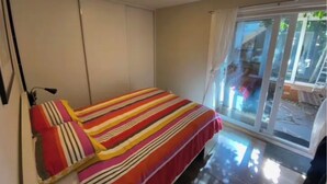 Un dormitorio con cama, una lámpara en el techo, una puerta corrediza de vidrio y vistas al exterior.