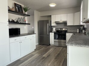 A modern kitchen with white cabinets, stainless steel appliances, and a wooden floor. - Extended Stay near HAFB in Roy (Roy)