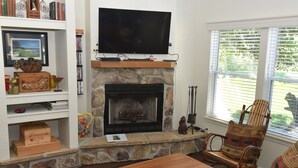 Una sala de estar con chimenea de piedra, un televisor de pantalla plana, muebles de madera y una estantería.