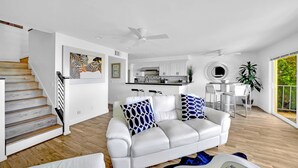 A modern living room with a white leather sofa, a staircase, a kitchen, and a dining area. - • Book HARBOR VIEW • Luxury 3BR • Panoramic Ocean & Harbor Views (Dana Point)