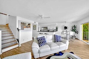 A modern living room with a white leather sofa, a staircase, a kitchen, and a dining area. - • Book HARBOR VIEW • Luxury 3BR • Panoramic Ocean & Harbor Views (Dana Point)