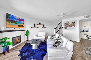Una sala moderna con chimenea, sofá de cuero blanco y un televisor grande.