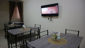 Zona pranzo con quattro tavoli, ognuno con un sottopiatti e una piccola pianta. Un televisore a schermo piatto è montato sulla parete sopra i tavoli.