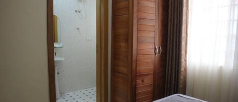 A bedroom with a wooden wardrobe, a bed with a grey blanket, and a bathroom with a shower.