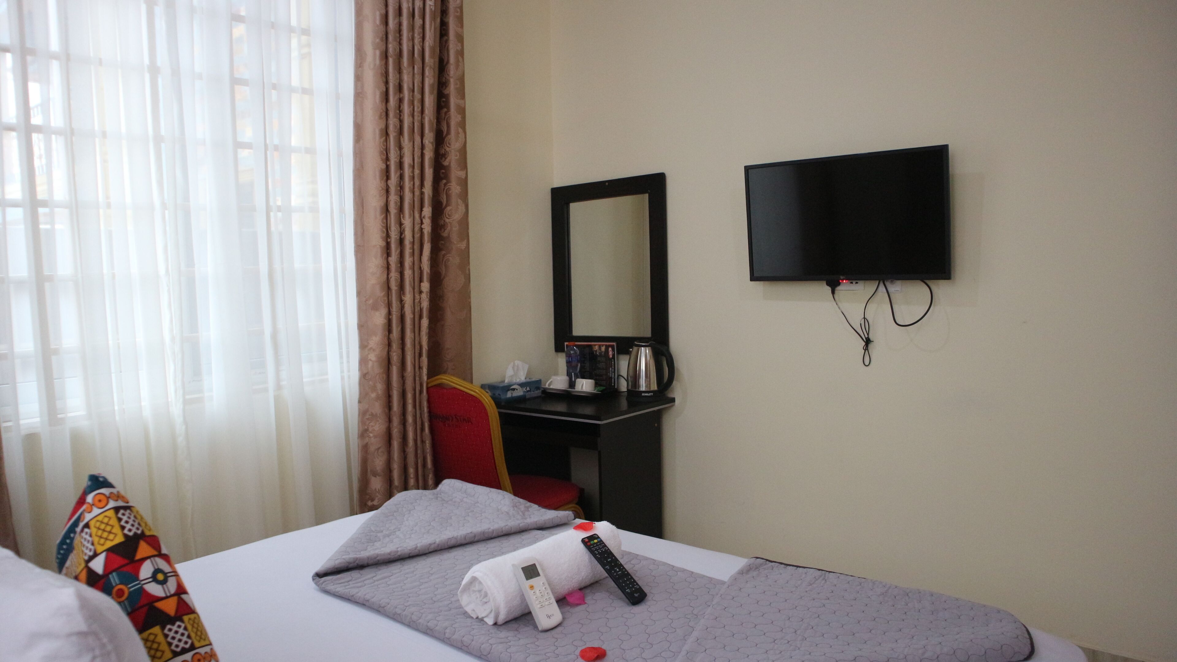 A hotel room with a bed, a desk, a television, and a window with curtains.