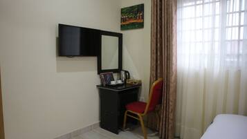 A hotel room with a bed, a desk with a chair, a television, a painting, and a window with curtains.