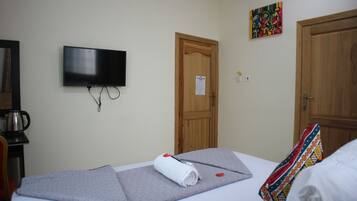 A hotel room with a bed, a television mounted on the wall, a wooden door, and a colorful artwork above the door.