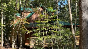 Eine Hütte, umgeben von Bäumen, mit einem begrünten Dach und einer Holzterrasse.