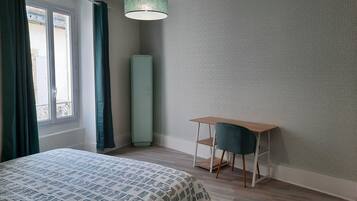 Quarto com cama, escrivaninha, cadeira, luminária pendente e parede estampada.