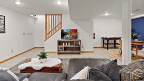 Un salon avec un canapé, un téléviseur posé sur un meuble en bois, un escalier et une table de baby-foot.