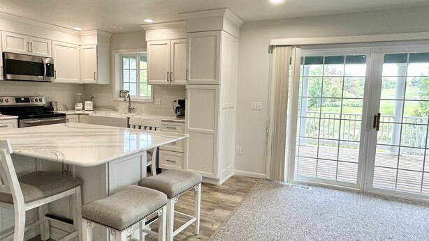 A modern kitchen with white cabinetry, a central island with bar stools, and a large sliding glass door leading to a deck.