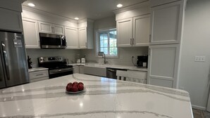 A modern kitchen with white cabinets, stainless steel appliances, and a marble island with a bowl of apples.