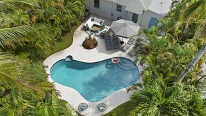 Ein von üppiger Vegetation umgebener Pool mit einer Terrasse, die Gartenmöbel und einen überdachten Sitzbereich bietet.