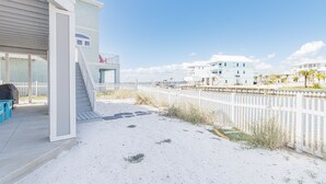 Ein Strandgrundstück mit überdachter Terrasse, einer Treppe, die zu einem Balkon führt, und einem weißen Zaun entlang des Strandes.