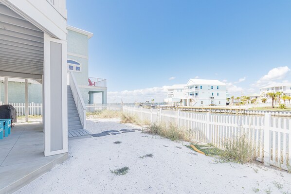 A beachfront property with a covered patio, a staircase leading to a balcony, and a white fence along the beach. - Hart’s Landing-Canal Front Home (Navarre)