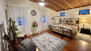 A bedroom with a wooden ceiling, a bed with a headboard, a bedside table with a lamp, a clock on the wall, and a window with curtains. - Cozy Cabin Natural Bridge VA (Natural Bridge Station)