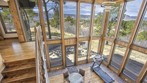 A spacious room with large windows offering a view of the outdoors, a wooden staircase, and a seating area with a table and chairs.