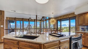A kitchen with wooden cabinets, a granite countertop, a sink, a stove, and large windows offering a mountain view.