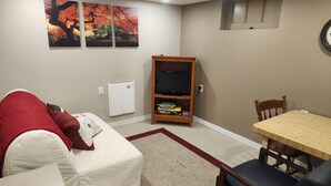 Una sala de estar con un sofá blanco, un mueble bajo para televisor de madera con un televisor de pantalla plana, una mesa de comedor con sillas y una alfombra roja.