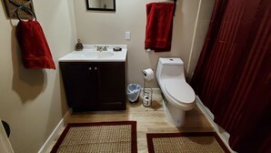 Un baño pequeño con un lavamanos blanco, armarios oscuros, un inodoro y un perchero rojo.