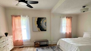 A bedroom with a bed, a ceiling fan, a window with curtains, a painting on the wall, and a small bench. - Beautiful contemporary 2BDR - Concord (Concord)