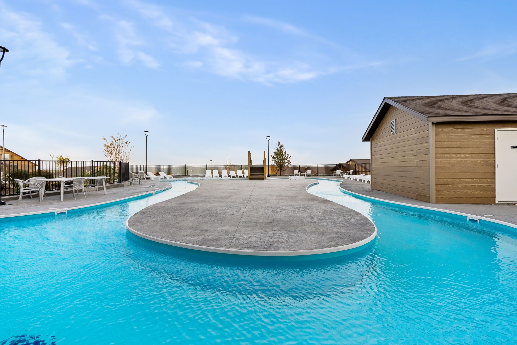 A swimming pool with a circular deck, lounge chairs, and a wooden building.
