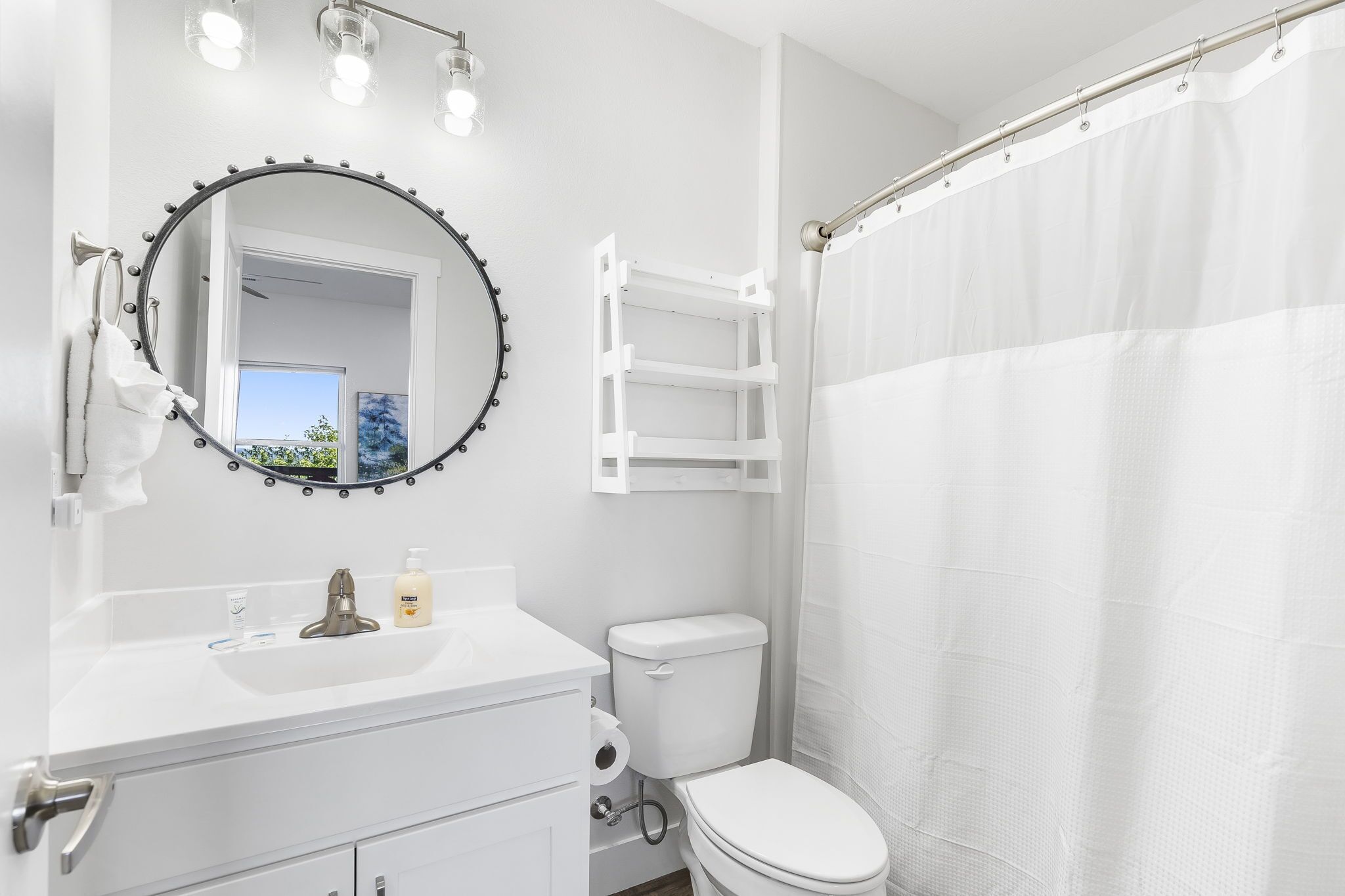 Une salle de bain avec un miroir rond, un meuble-lavabo, des toilettes et un rideau de douche.